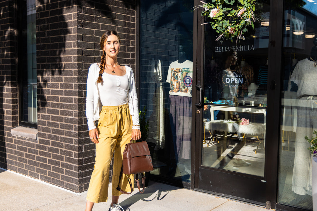 Uliana Leon wears mustard wide-leg pants and carries a brown backpack by Bella Emilia Boutique.